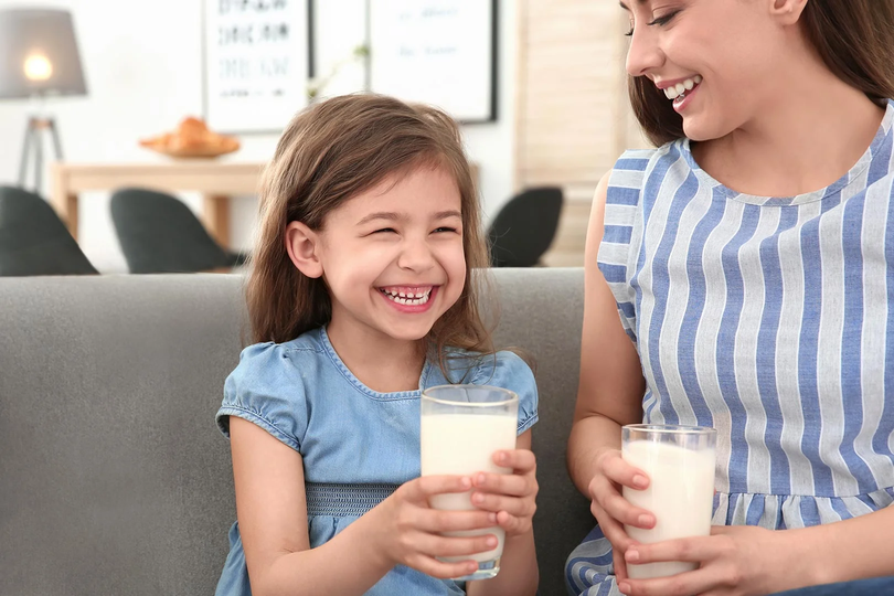 Mamá e hija alegre tomando un vaso con leche KLIM®. 