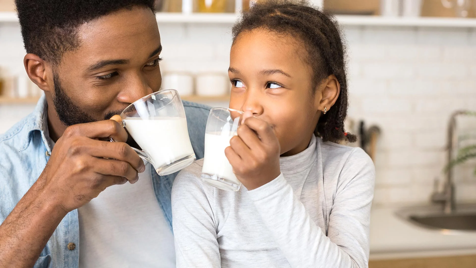 Papá e hija alegre disfrutando de los beneficios de un vaso de leche KLIM®. 
