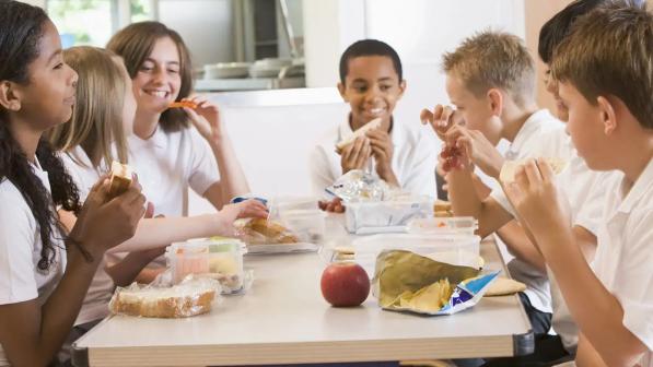 Tres niñas y tres niños comiendo snacks y compartiendo una mesa